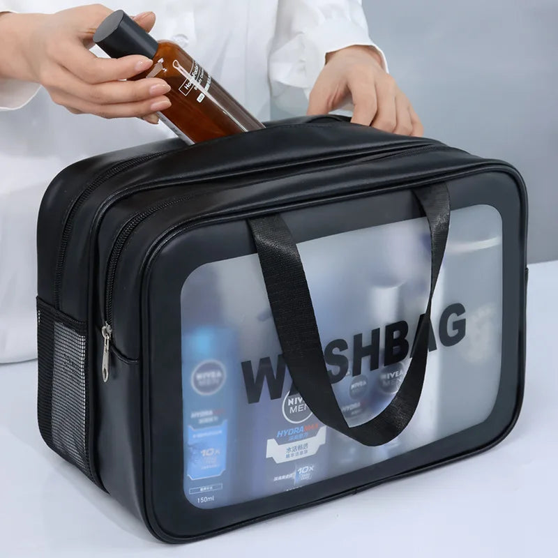 Black travel wash bag with clear window showing toiletries, held by a person.